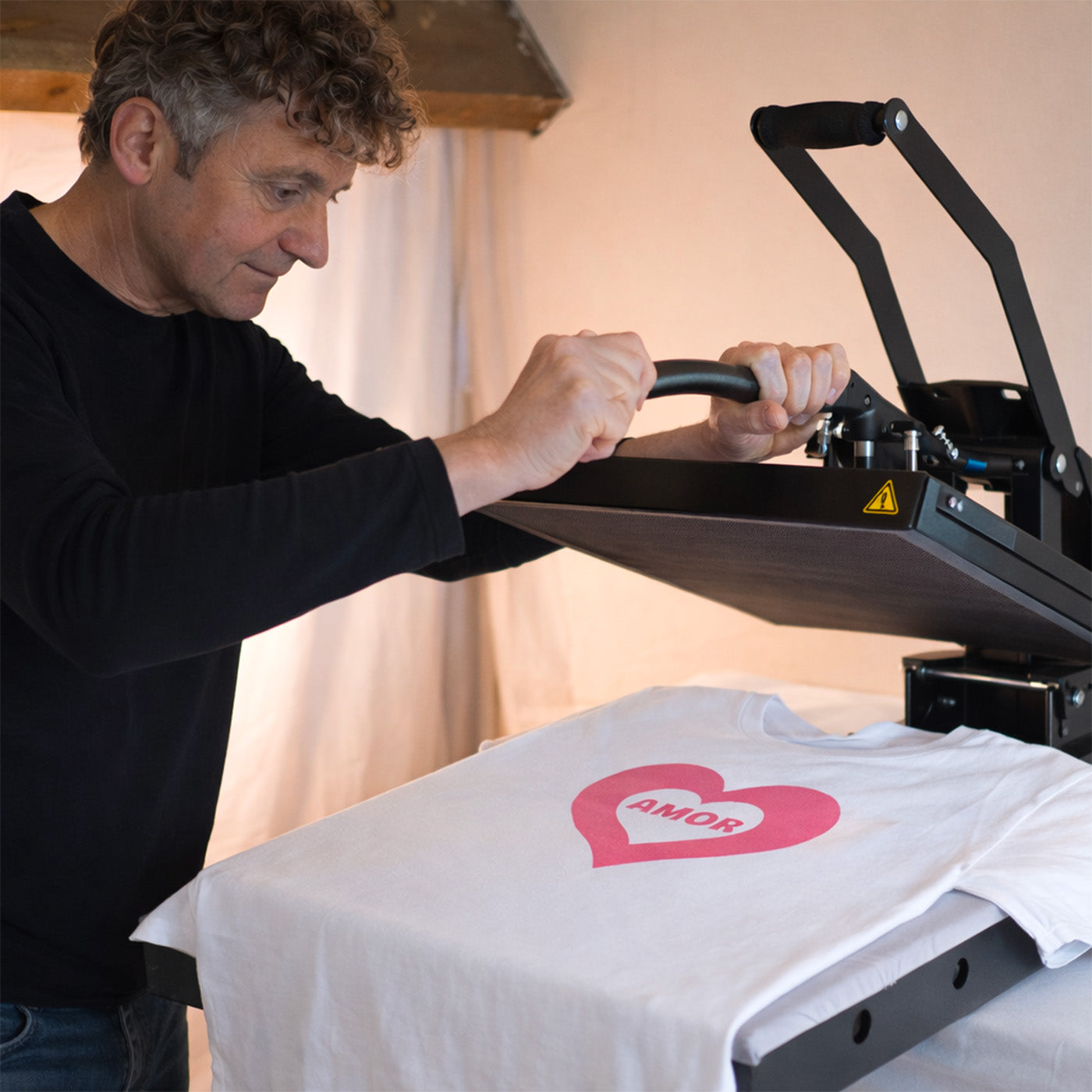 Homme réalisant le flocage d’un tee-shirt blanc avec cœur rose Amor en atelier de personnalisation textile