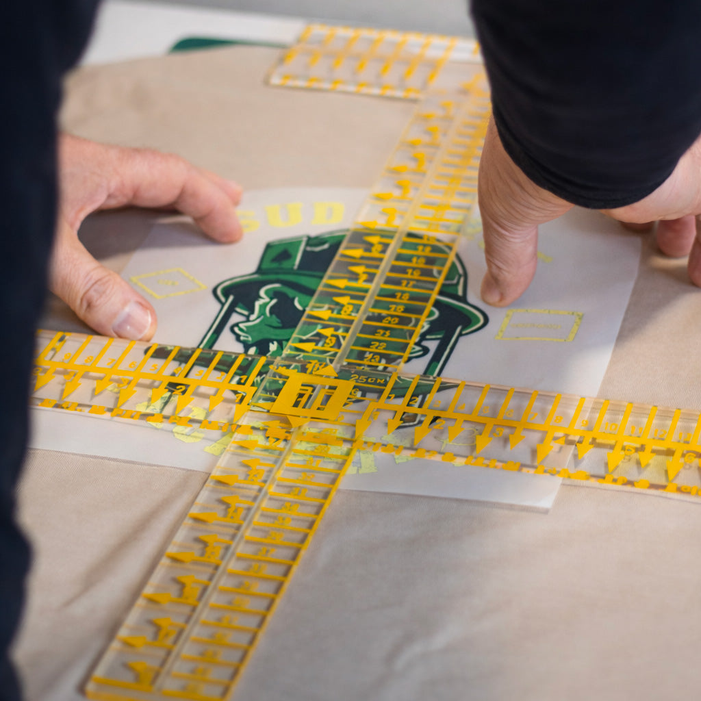 Positionnement précis d’un visuel Sud Ouest Academy sur un t-shirt beige en atelier, avant impression textile.