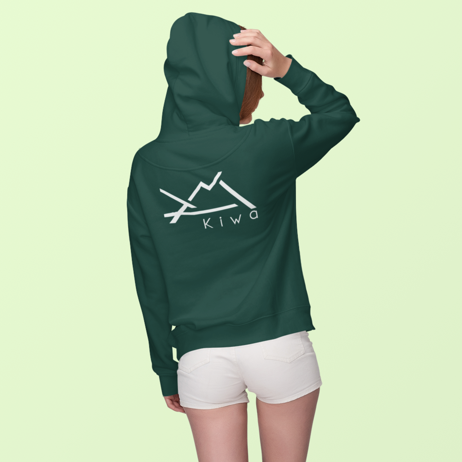Sweat à capuche vert KIWA porté par une femme, logo montagne blanc dans le dos, vêtement outdoor sud-ouest.